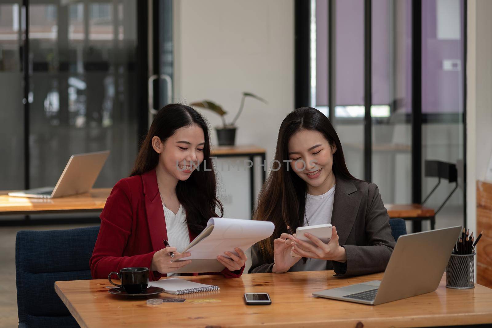 Two asian female colleagues sitting next to each other in an office, business meeting discussion concept by nateemee