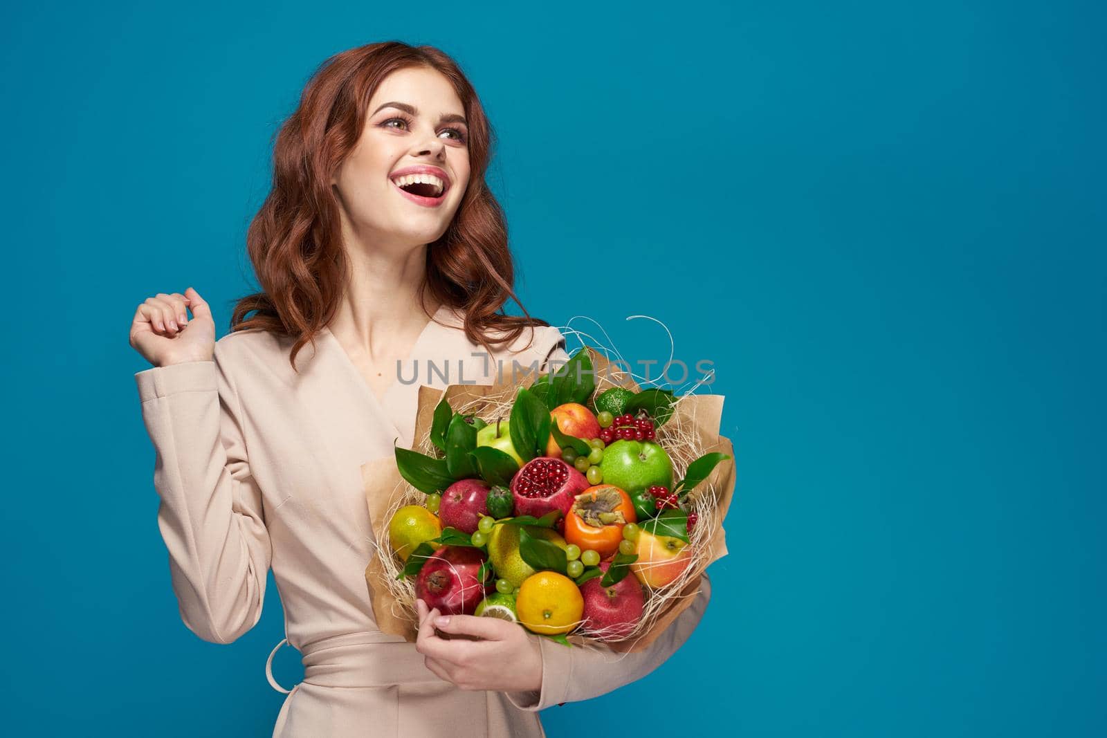 beautiful woman beige coat fruit bouquet in hands blue background. High quality photo