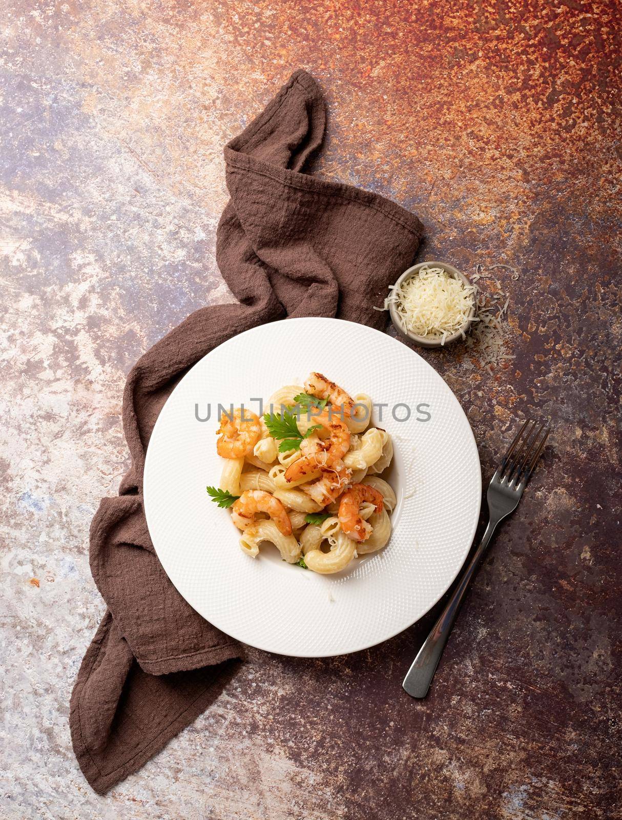 Italian cuisine. pasta with bechamel sauce with green shrimps, cheese and parsley in while plate on dark background, top view copy space