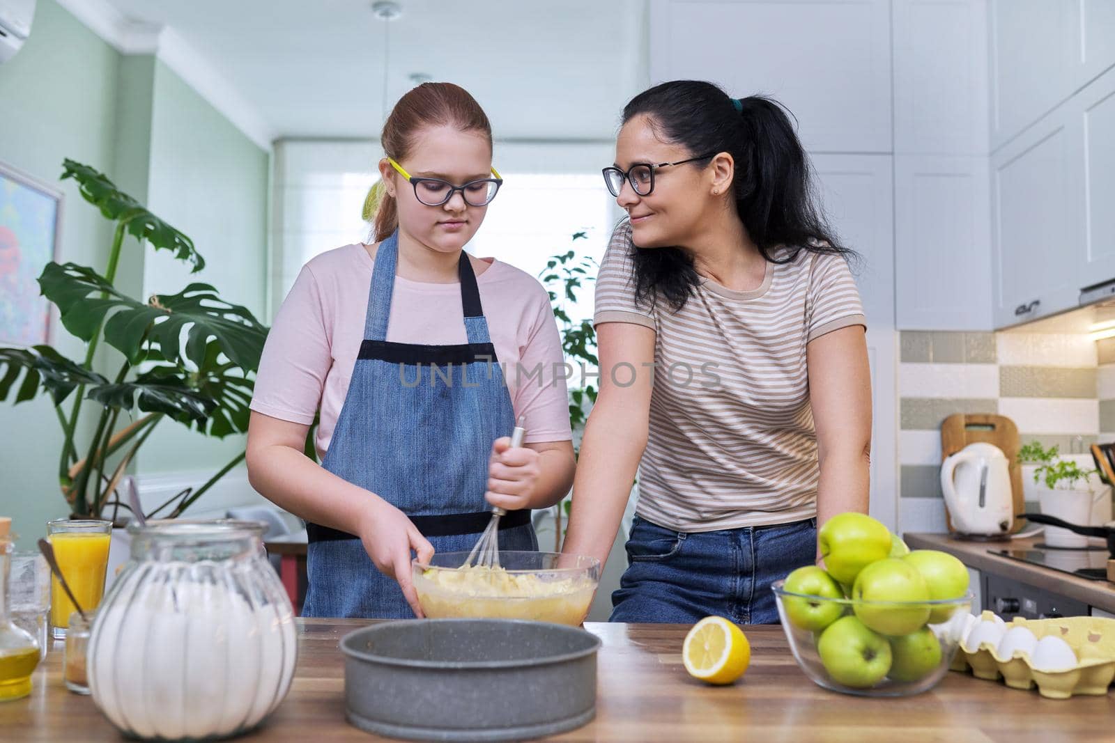 Mom and teenage daughter preparing apple pie together, at home in the kitchen. Family, parent teenager relationship, lifestyle, eating at home concept
