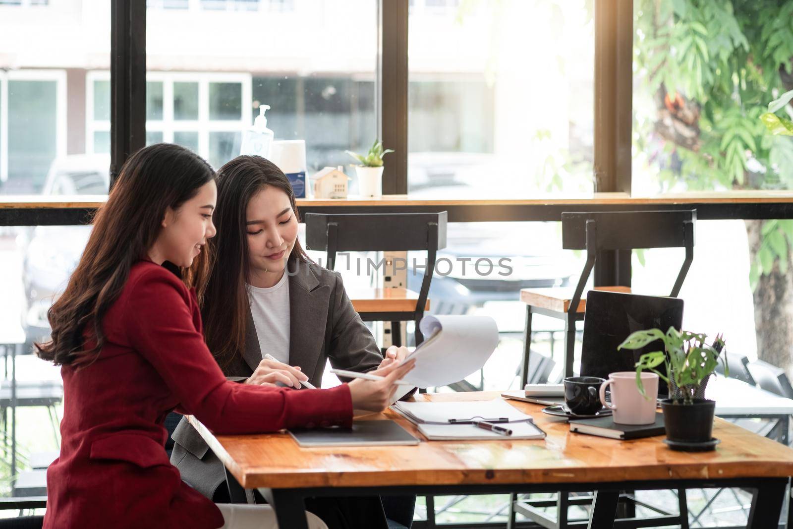 Young and partnership holding a pen pointing the graph to analyze the marketing plan with calculator and laptop computer on wood desk in office.