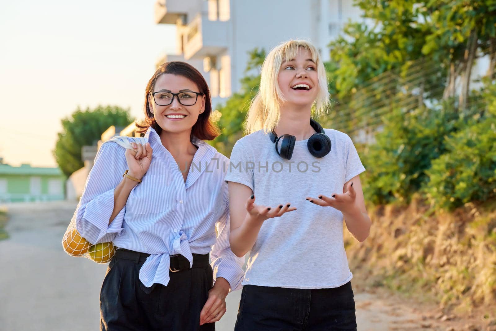 Beautiful talking mom and teenage daughter outdoors. Happy mother and teen girl walking together with eco shopper with oranges. Family, happiness, relationship parent teenager, summer, trendy, people