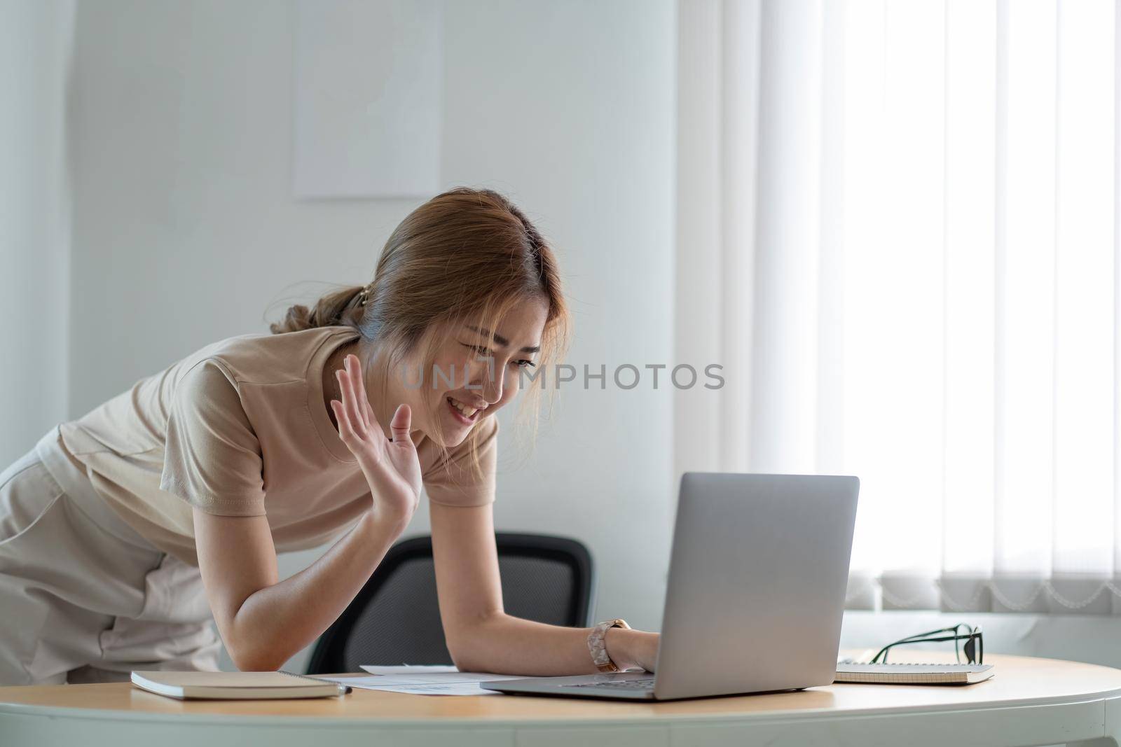 Pretty casual girl waving hand to video call using laptop at home.