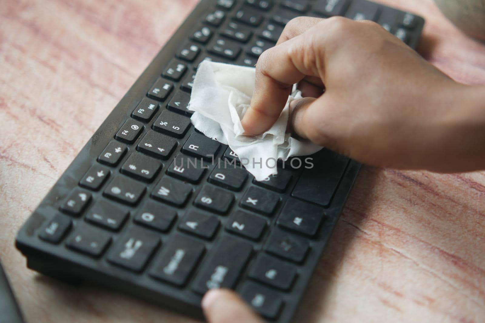 disinfecting keyboard with a white tissue on table .