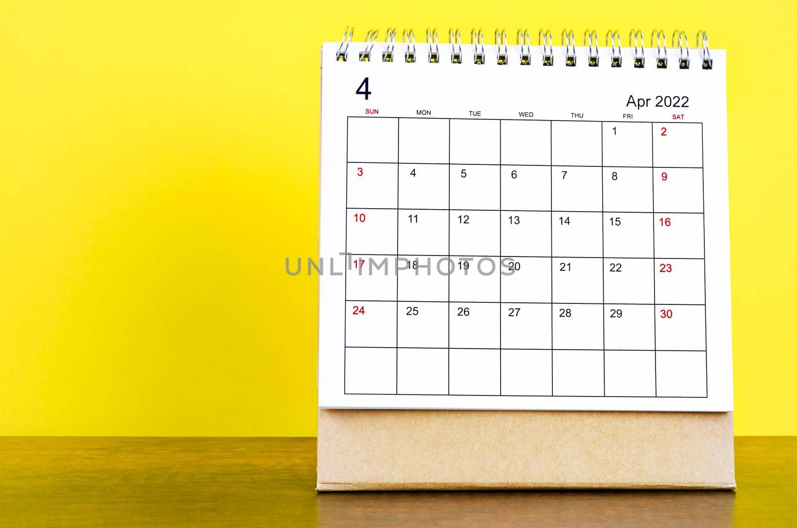 The April 2022 desk calendar with yellow background on the wooden table.