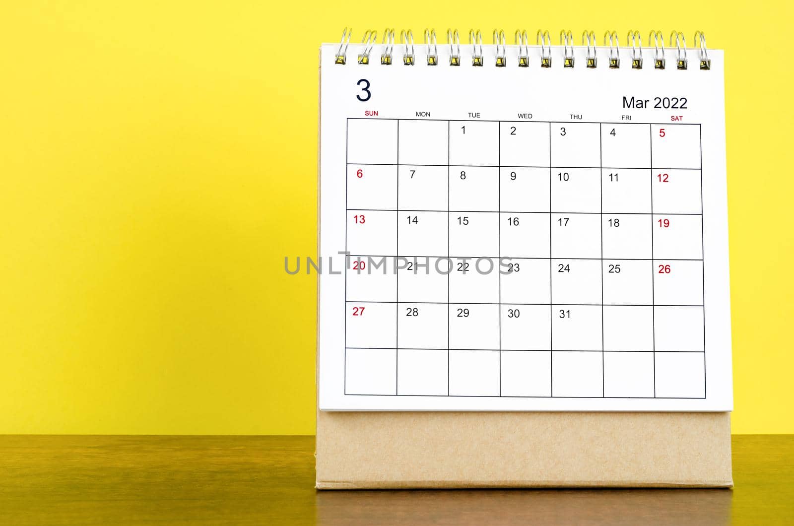 The March 2022 desk calendar with yellow background on the wooden table.