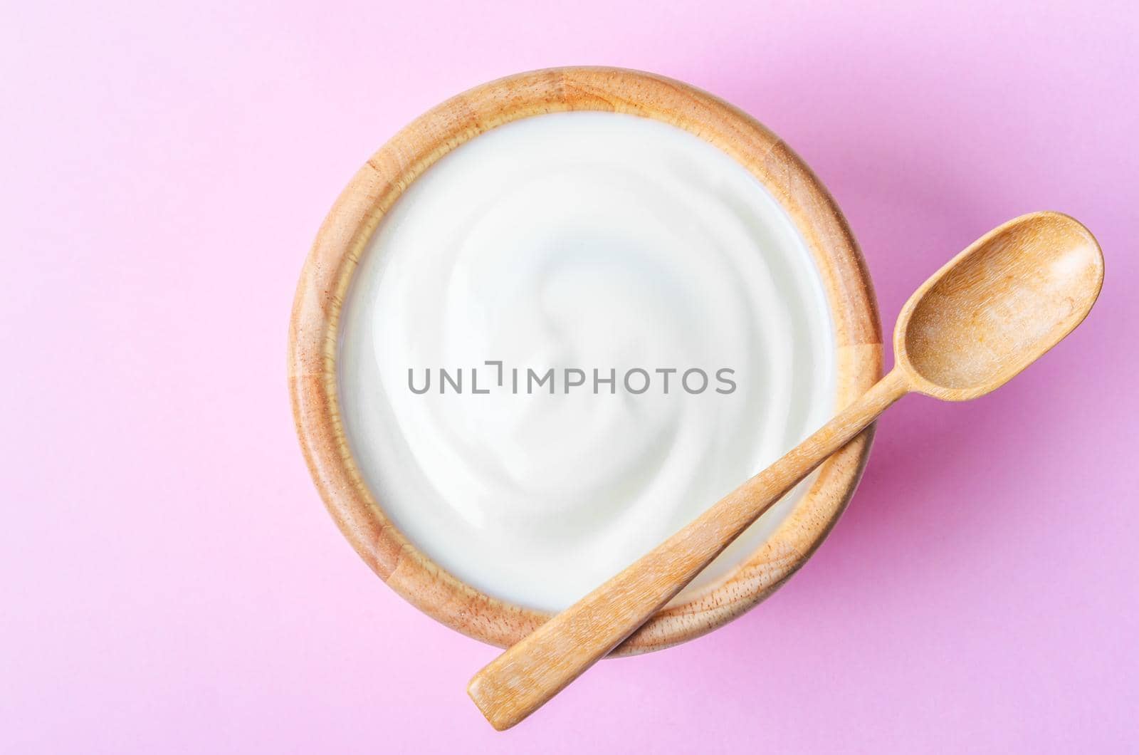 Greek yogurt with wooden spoon in a wooden bowl on pink background.