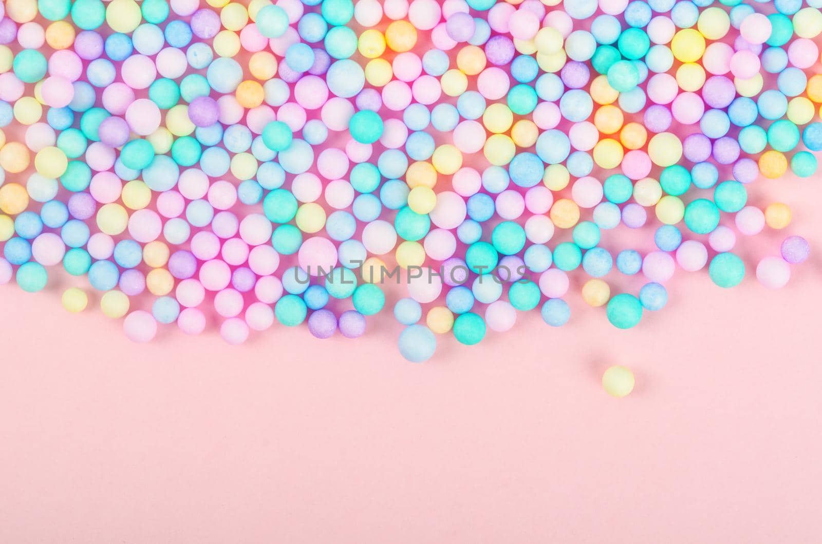 Foam beads of various colors brightly colored on pink pastel background with empty space.