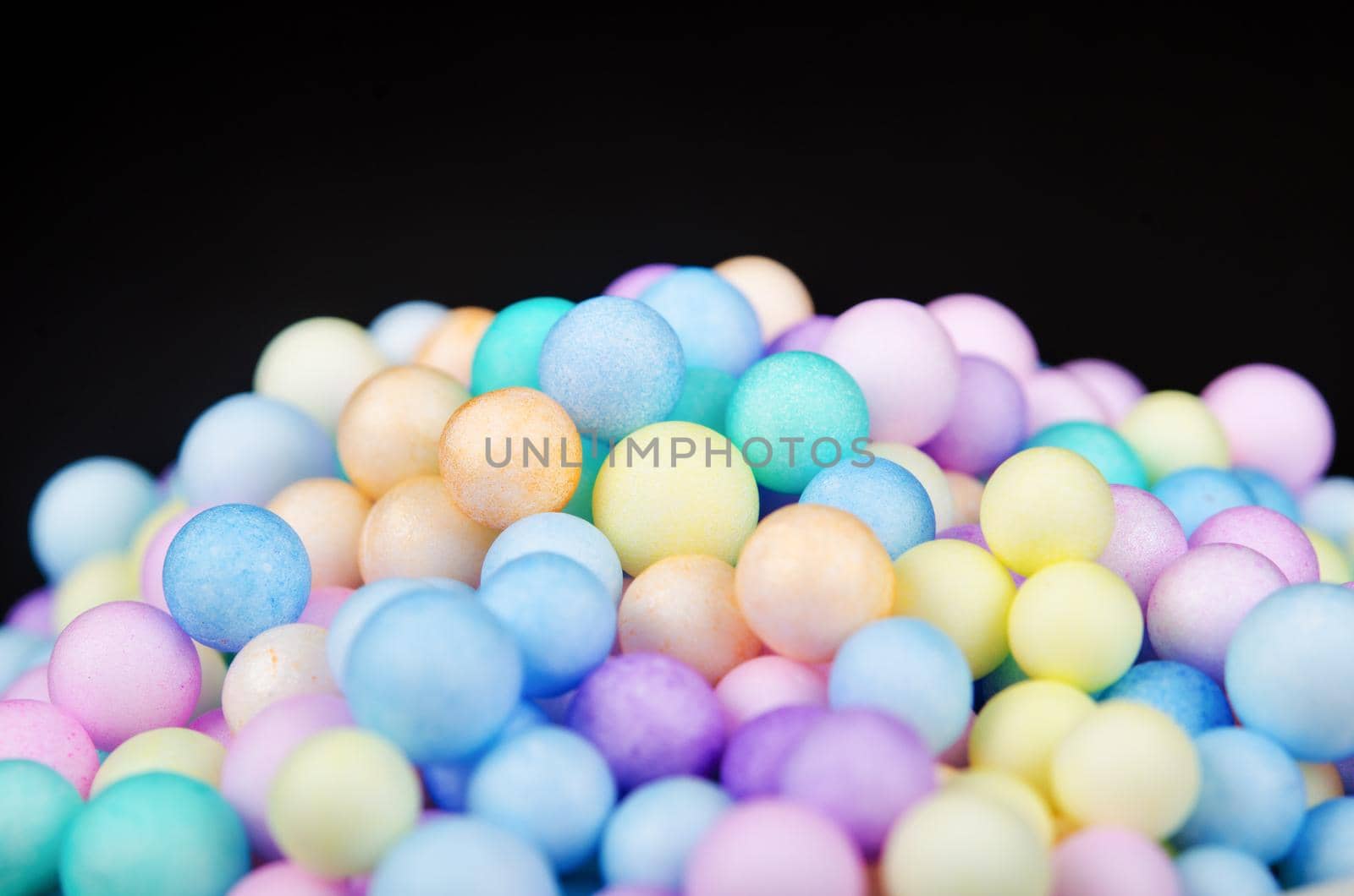 Foam beads of various colors brightly colored on black background.