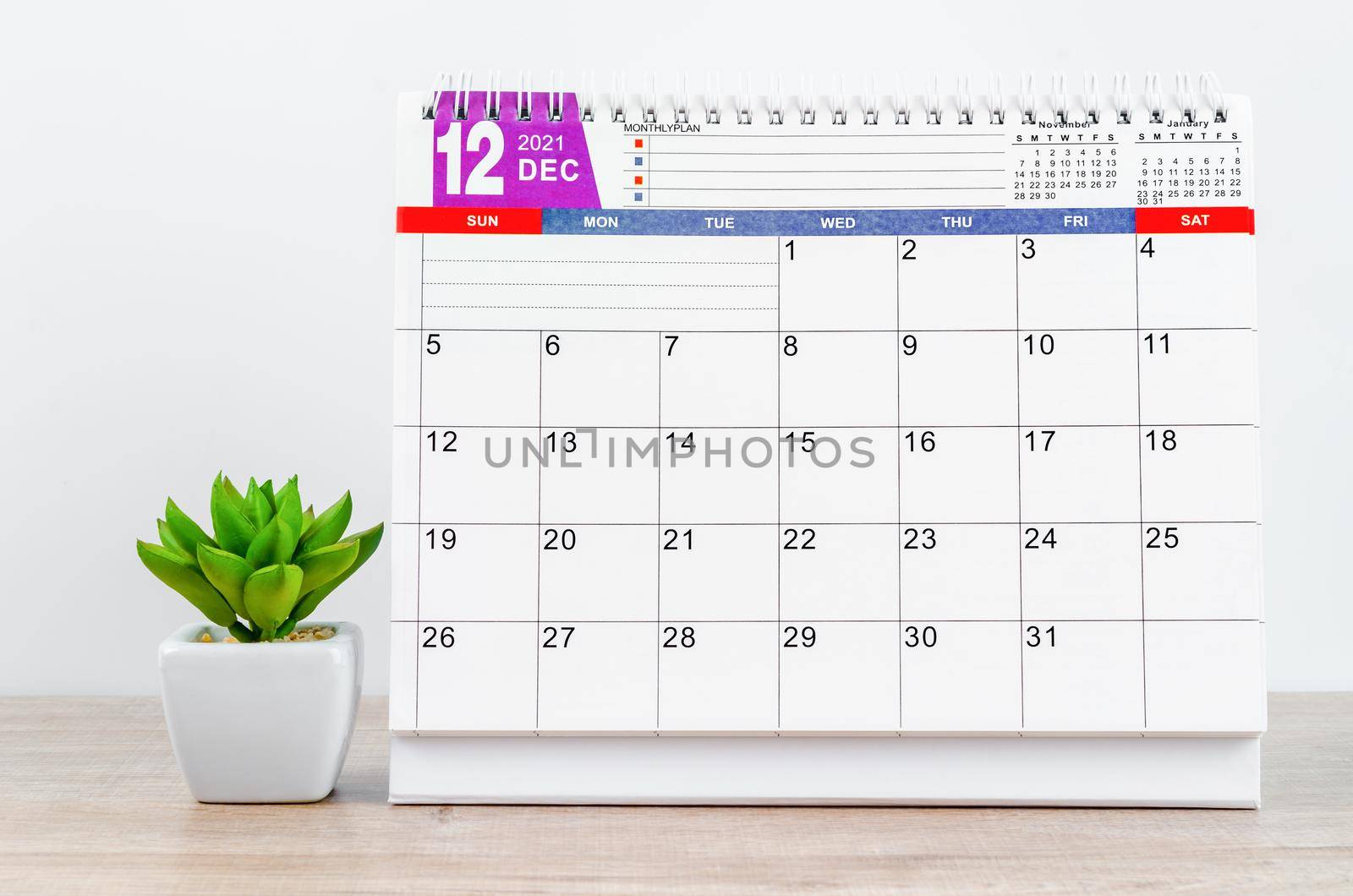 December 2021 desk calendar with plant in pot on wooden table.