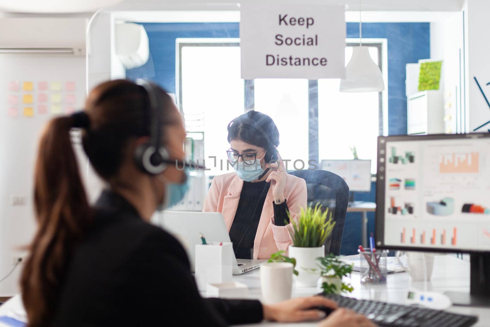 Businesswoman discussing business partnership with manager using headphones working at financial presentation in startup corporate office. Entrepreneur wearing medical face mask against covid19