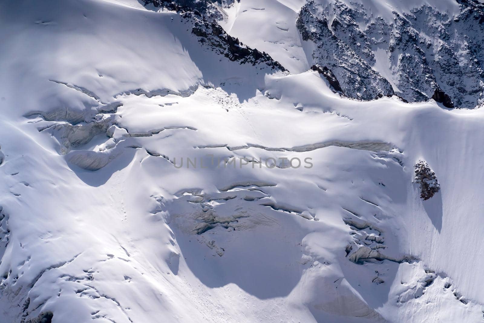 Harsh majestic landscape with snow-capped mountains, glacier and ice cracks covered with snow on a sunny day.
