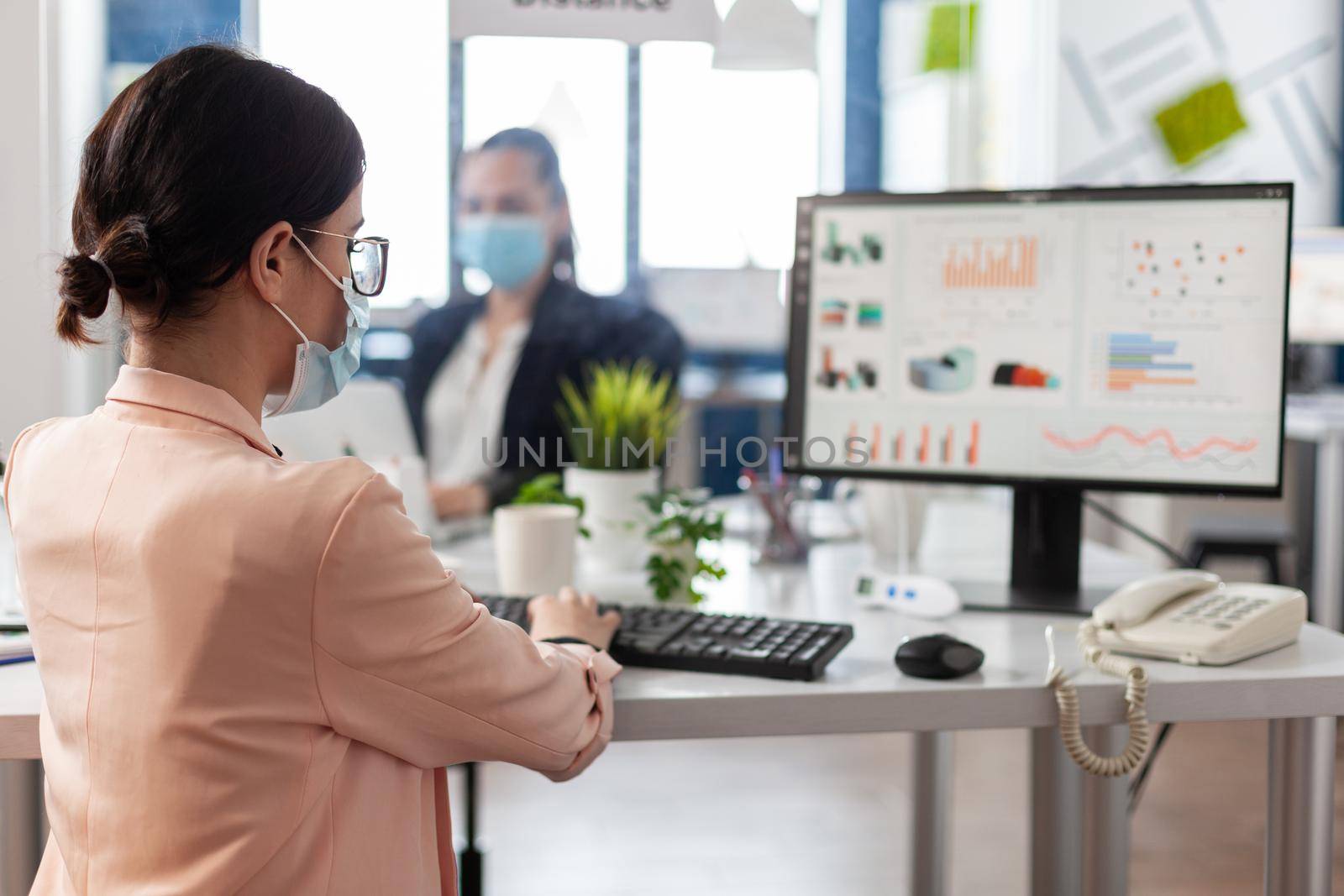 Businesswoman typing company strategy on computer working at management presentation in startup corporate office. Business team wearing medical face mask to prevent infection with coronavirus