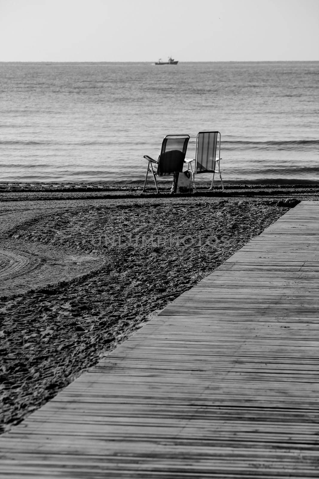 Lonely beach chairs on the shore and wooden walkway to the Levante Beach in Spain