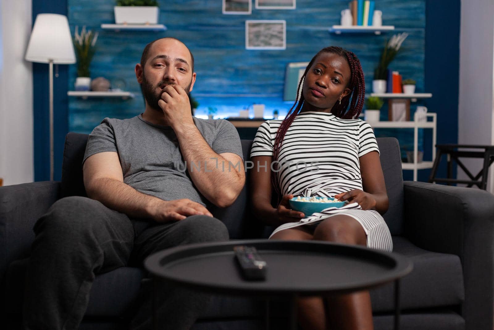 POV of interracial couple watching television enjoying activity in living room. African american woman and caucasian man looking at camera while bonding, relaxing and eating popcorn