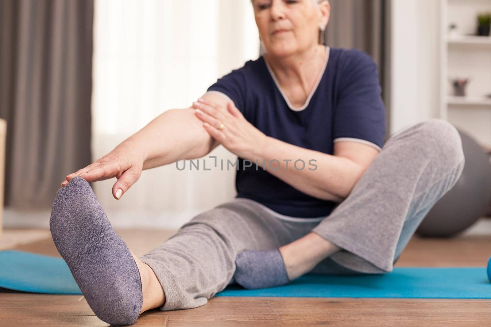 Modern grandmother doing stretching at home oon yoga mat. Old person pensioner online internet exercise training at home sport activity with dumbbell, resistance band, swiss ball at elderly retirement age
