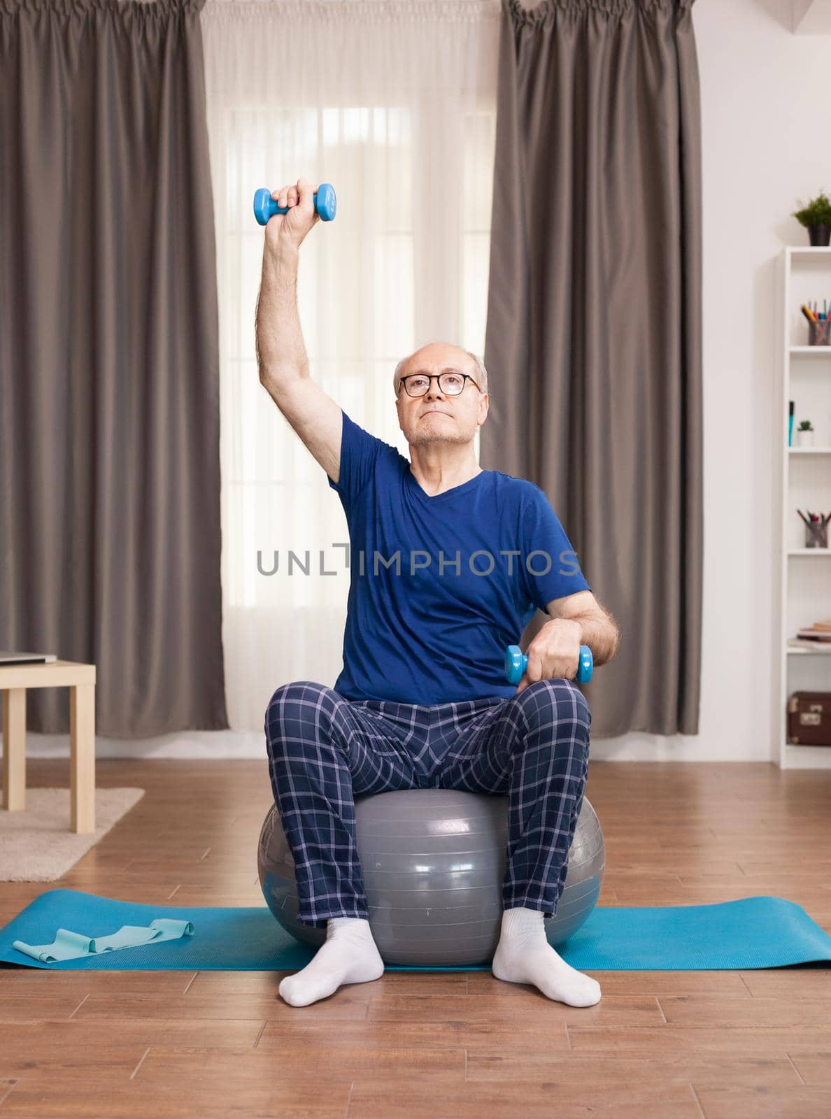 Senior man doing sports with weights. Old person pensioner online internet exercise training at home sport activity with dumbbell, resistance band, swiss ball at elderly retirement age.