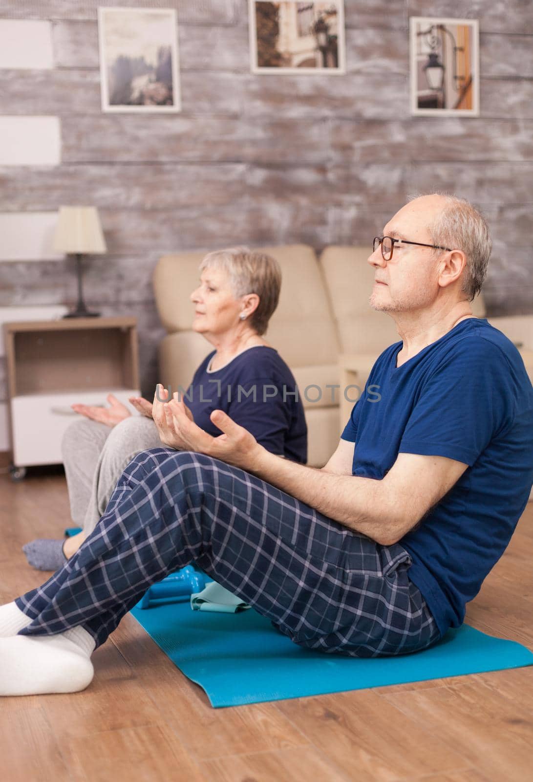 Retired people meditating on yoga mat in living room. Old person healthy lifestyle exercise at home, workout and training, sport activity at home on yoga mat.