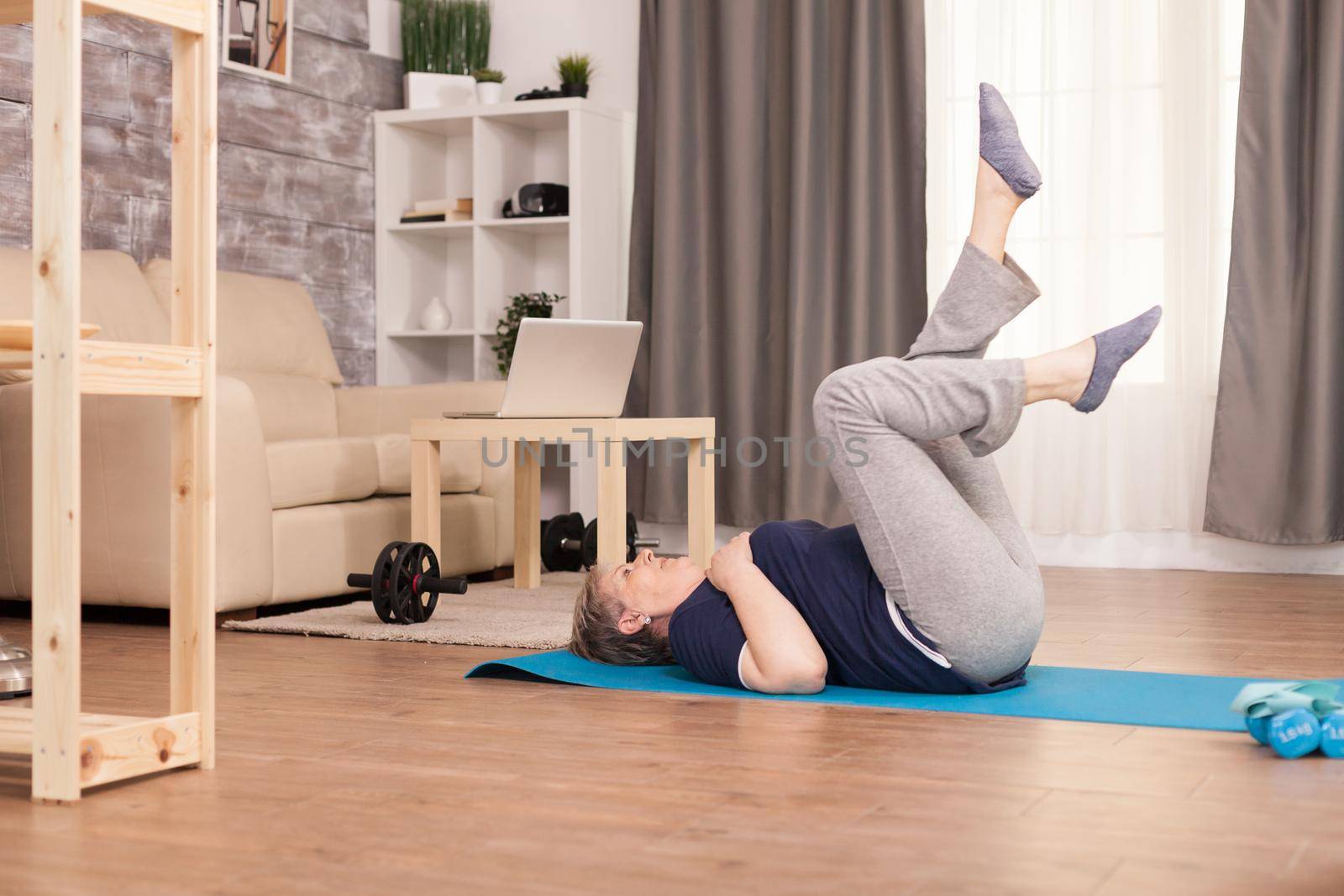 Senior woman doing abs physical training sitting on yoga mat. Old person pensioner online internet exercise training at home sport activity with dumbbell, resistance band, swiss ball at elderly retirement age