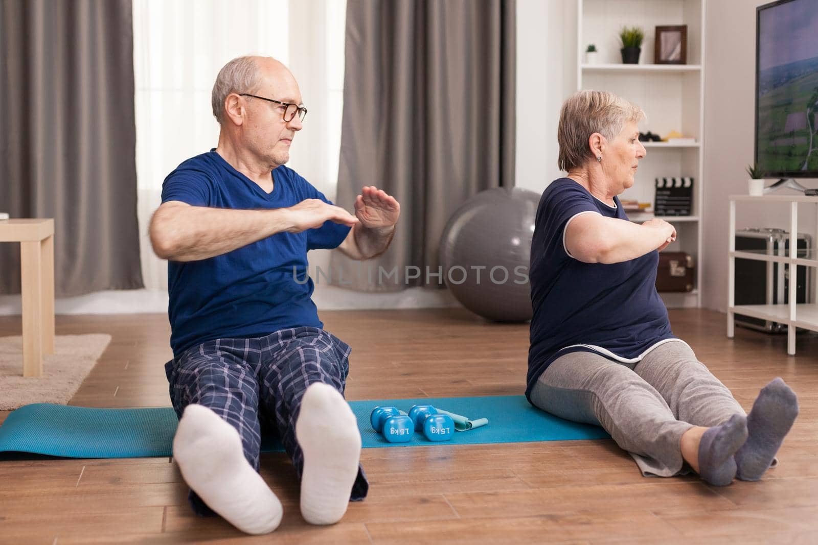 Active senior couple stretching their bodies. Old person healthy lifestyle exercise at home, workout and training, sport activity at home on yoga mat.
