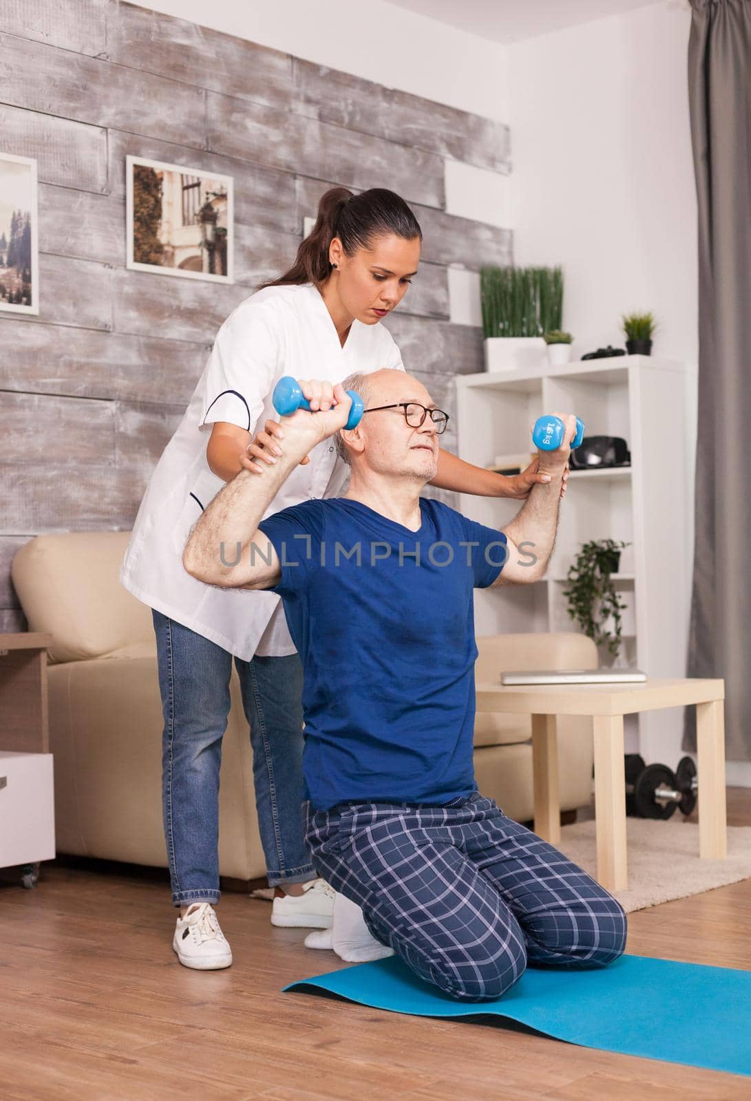 Doctor helping senior patient to exercise correctly using dumbbells. Home assistance, physiotherapy, healthy lifestyle for senior old person, training and recovery with professional physiotherapist.