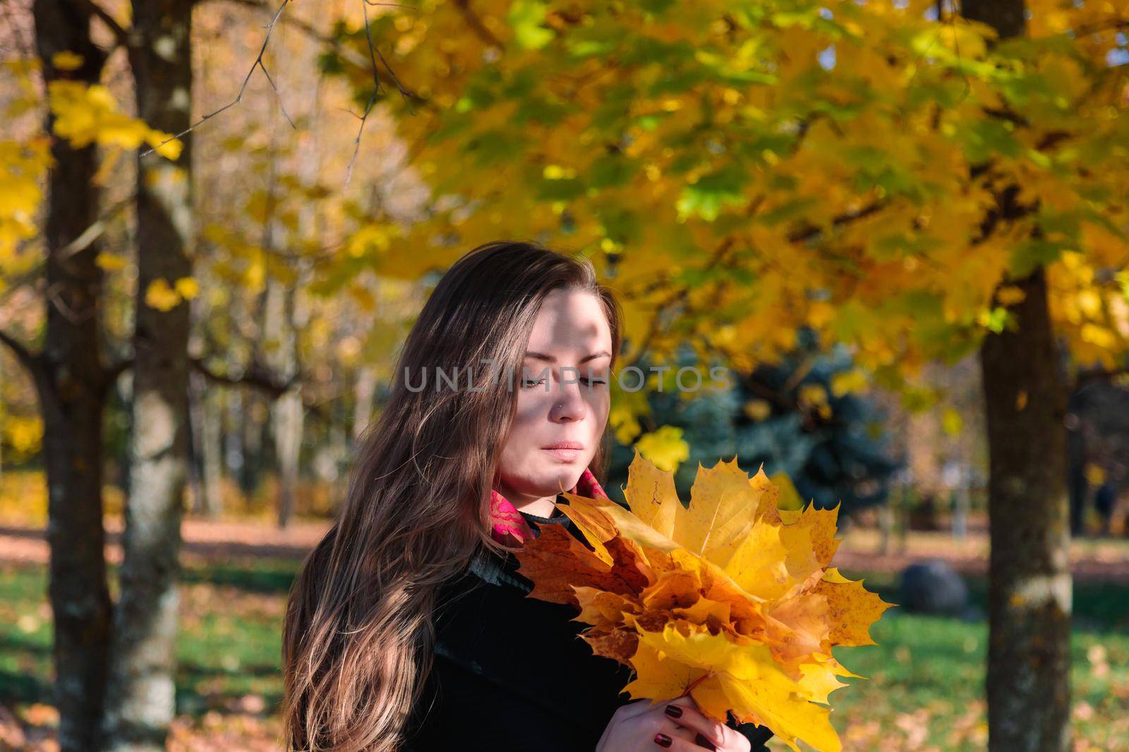 A woman with long hair looks at yellow leaves in an autumn park. Autumn season.