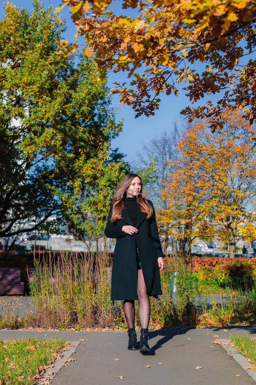 A woman with long hair walks alone along a path in an autumn park. Autumn season concept.