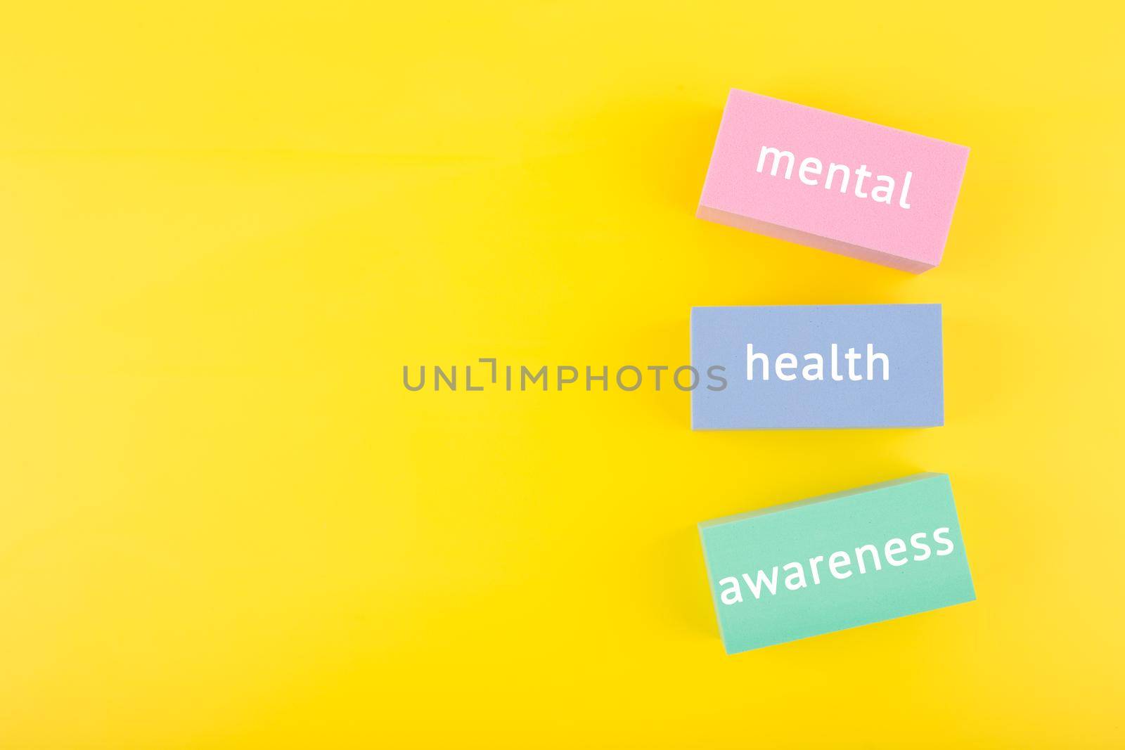 Mental health awareness concept on yellow background with copy space and with text written on colorful tablets. Concept of mental health, self care and psychological issues