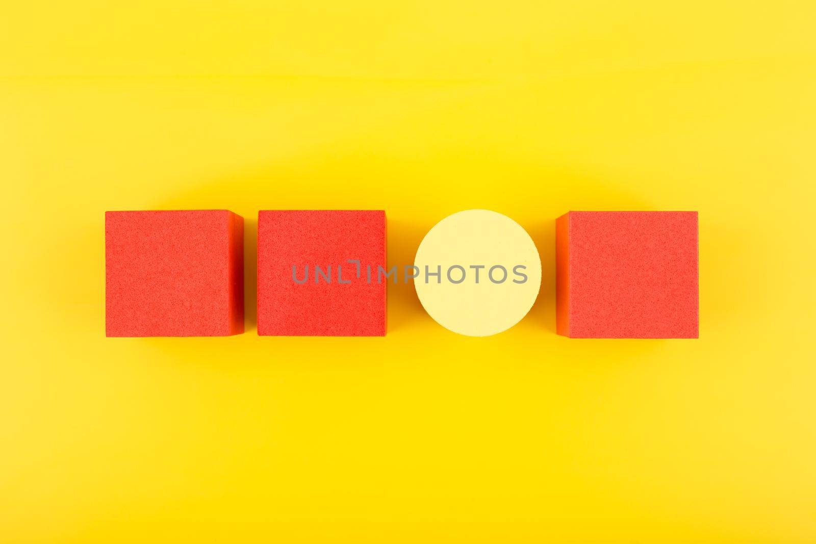 Red toy cubes and yellow circle in a row on bright yellow background. Concept of individuality, being different from others, leadership or unique ideas 