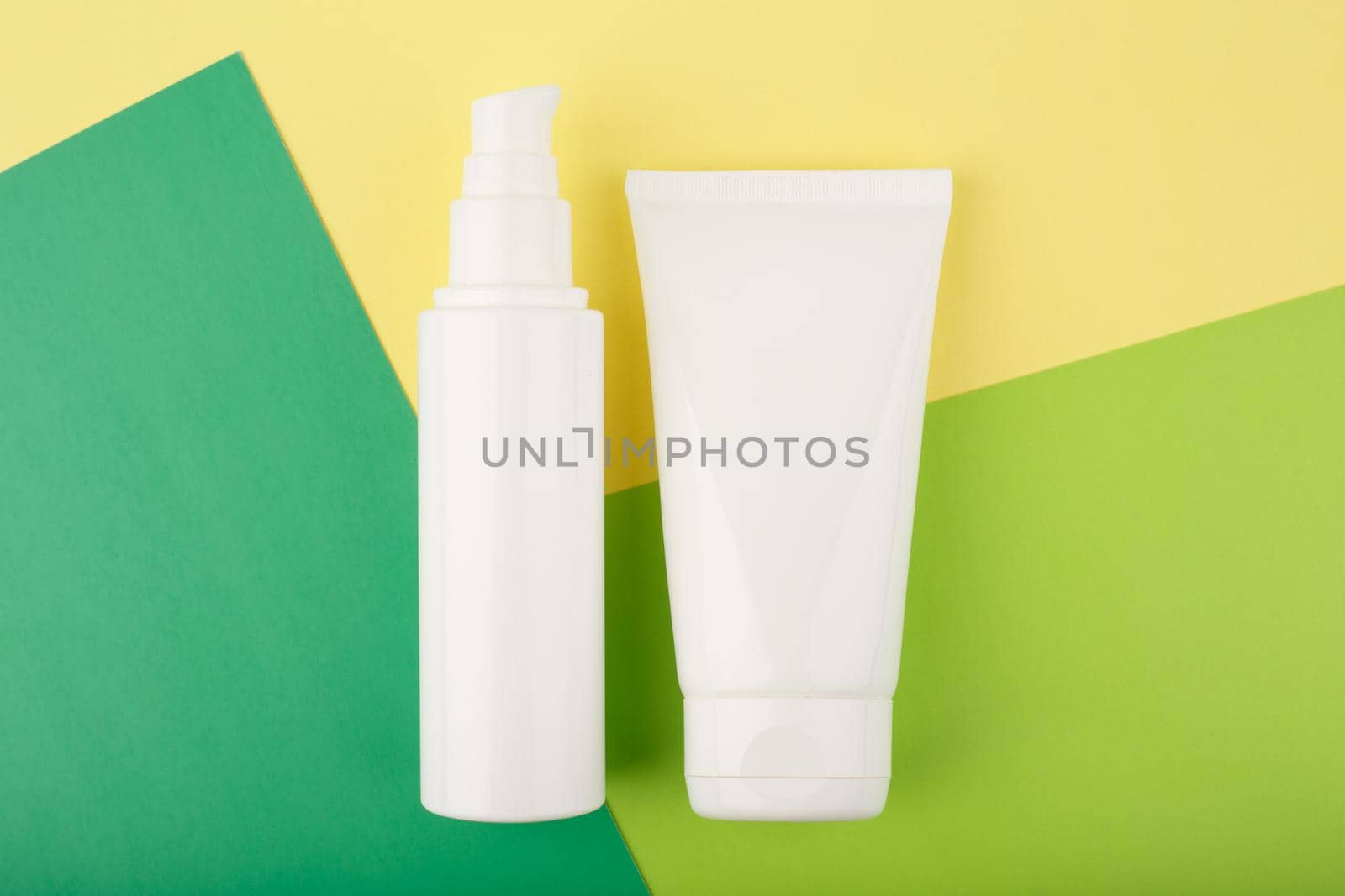 Flat lay with cosmetic products in white unbranded tubes on green and yellow paper  by Senorina_Irina