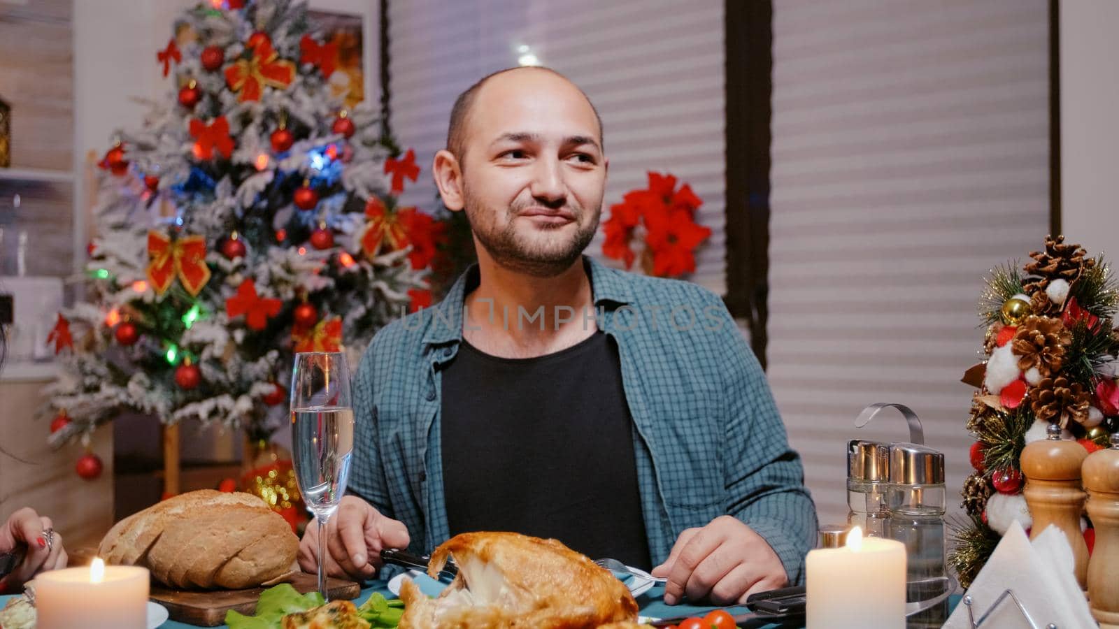 Close up of man talking on video call and waving while eating chicken with woman at festive dinner. Adult using online conference for remote communication, celebrating christmas eve.