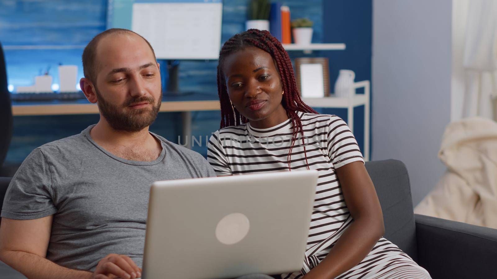 Young interracial couple waving at video call camera on laptop by DCStudio