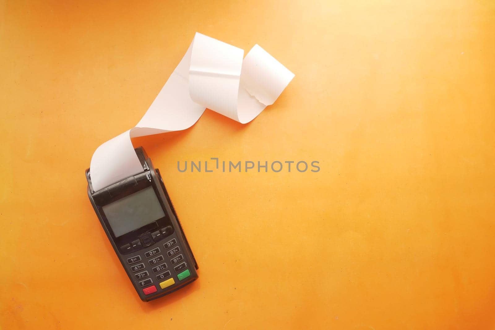 POS machine and long roll paper on orange background .