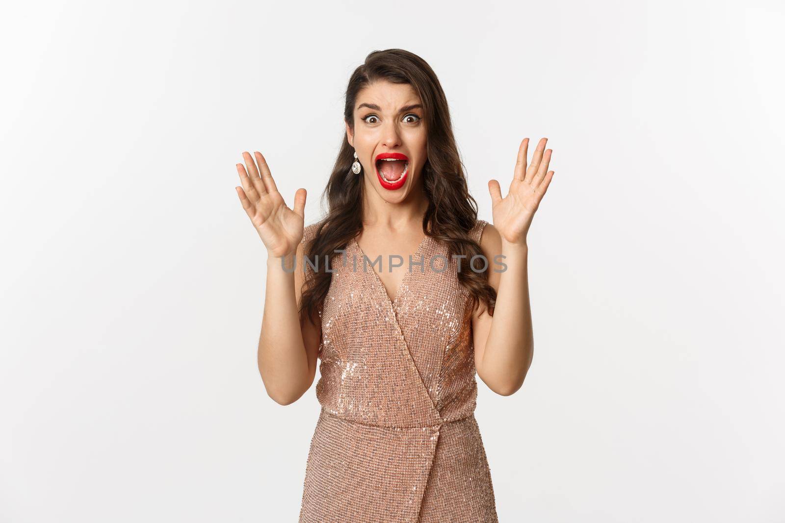Celebration and party concept. Beautiful woman in elegant dress screaming and staring at camera scared, looking at something scary, standing over white background.