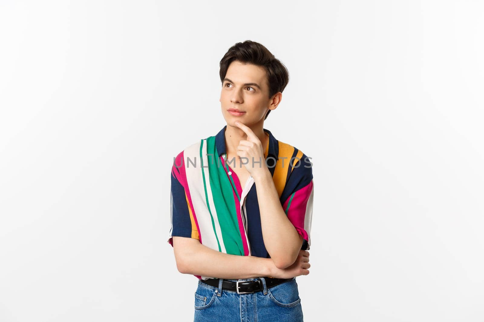 Portrait of thoughtful queer man in stylish shirt, looking at upper left corner and thinking, making choice, standing over white background.