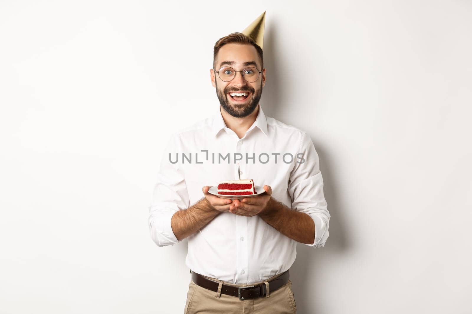 Holidays and celebration. Happy man having birthday party, making wish on b-day cake and smiling, standing against white background.