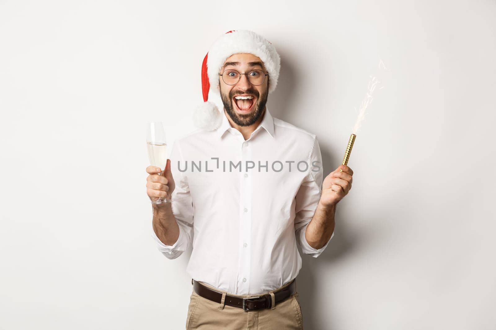 Winter holidays and celebration. Happy guy in Santa hat rejoicing at New Year party, drinking champagne and shouting of joy, white background.