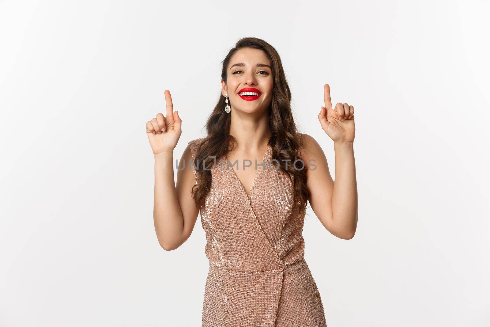 New Year, christmas and celebration concept. Gorgeous and elegant woman showing holidays advertisement, pointing fingers up, showing promo offer, standing over white background.