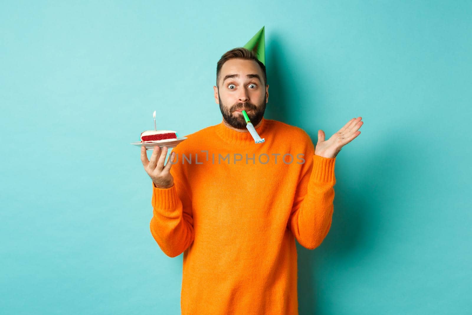 Happy birthday guy celebrating, wearing party hat, blowing wistle and holding bday cake, standing against white background by Benzoix