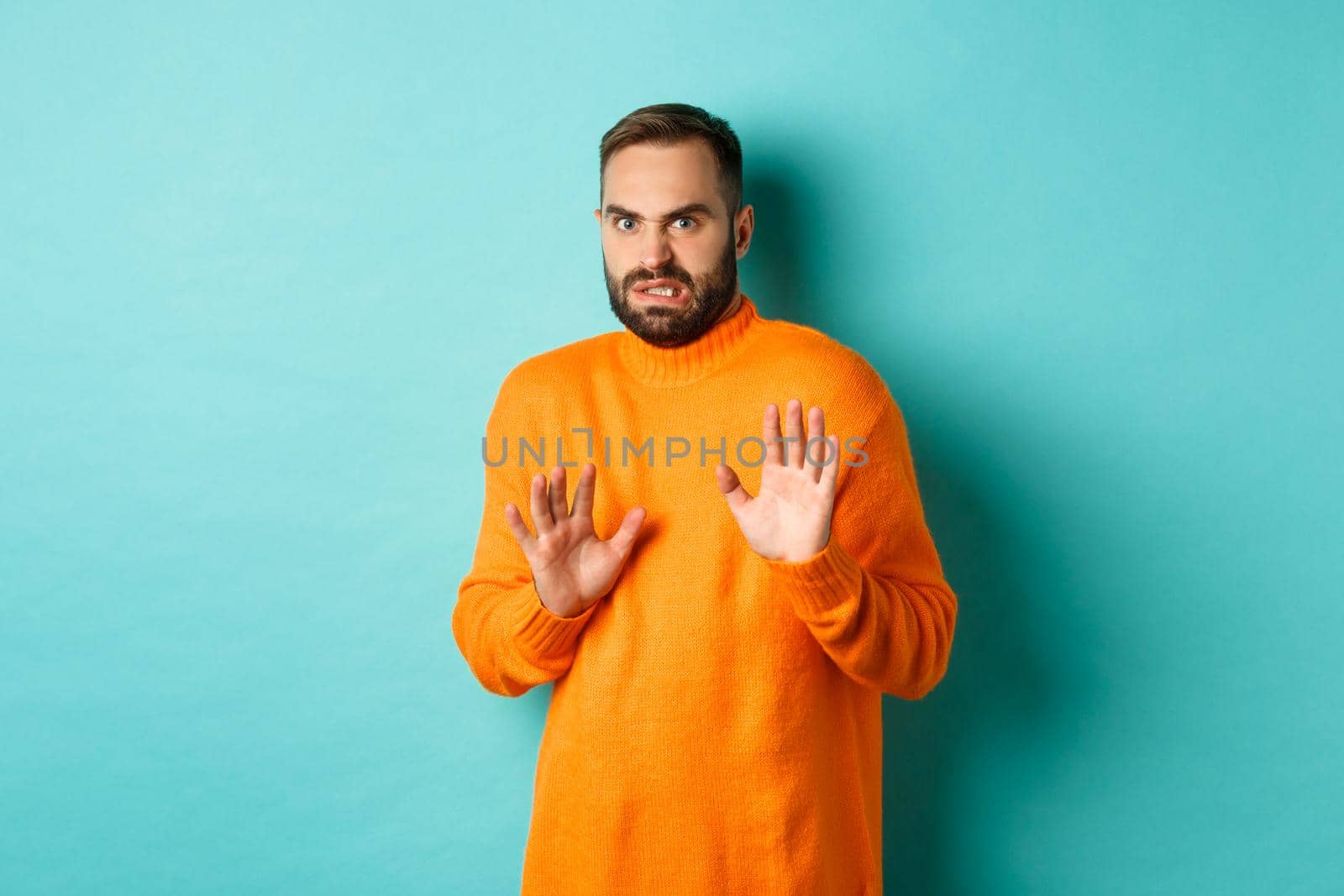 Alarmed guy shaking hands in rejection, declining and stepping away scared, standing over light blue background.