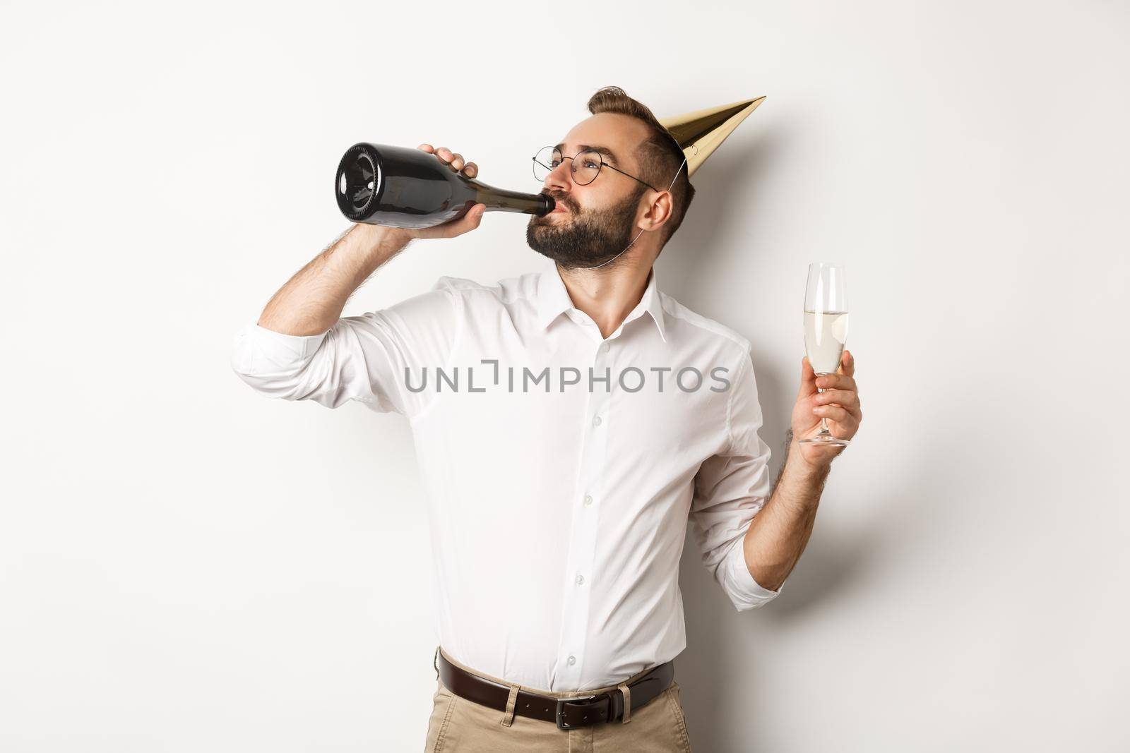 Celebration and holidays. Man drinking chamapgne from bottle on birthday party, standing against white background.