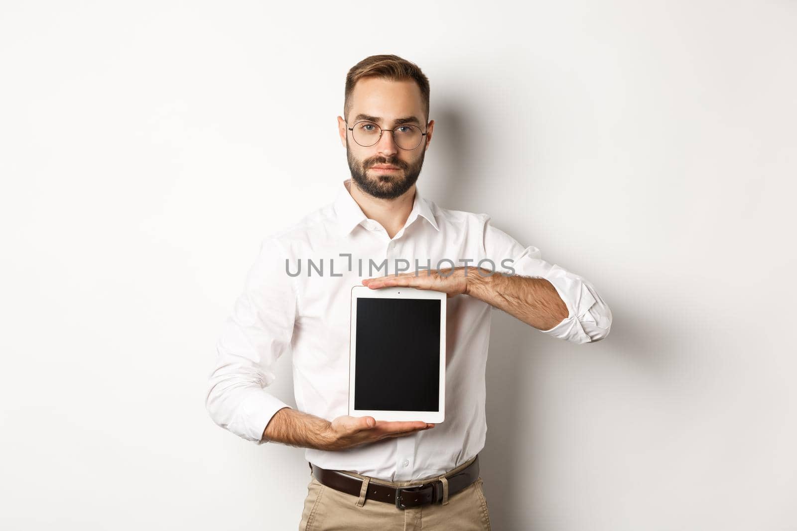 Confident bearded man showing digital tablet screen, demonstrating app, standing over white background.