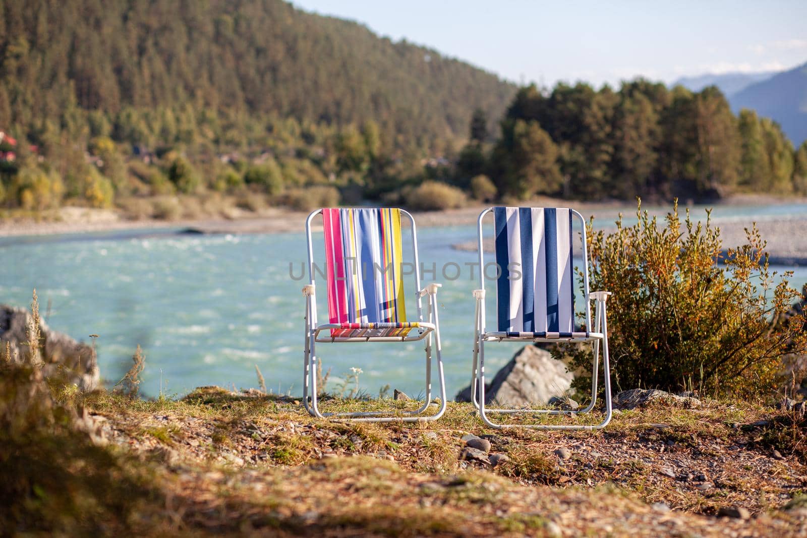 Folding chairs on the bank of a mountain river on a nice, warm day.  by AnatoliiFoto
