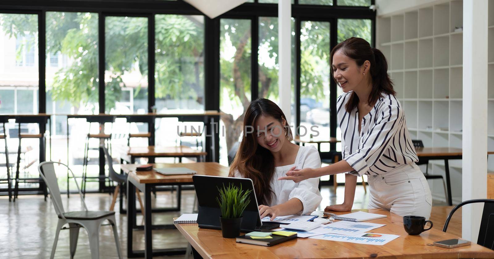 Friendly female colleagues having good relationships, pleasant conversation at workplace, smiling young asian woman listen talkative coworker, discussing new project, talking in office by nateemee
