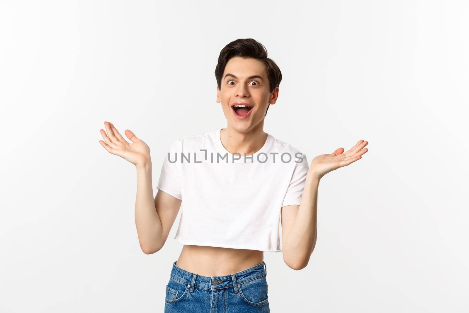 Lgbtq and pride concept. Handsome young man in crop top raising hands up and looking surprised, rejoicing of good news, standing over white background.