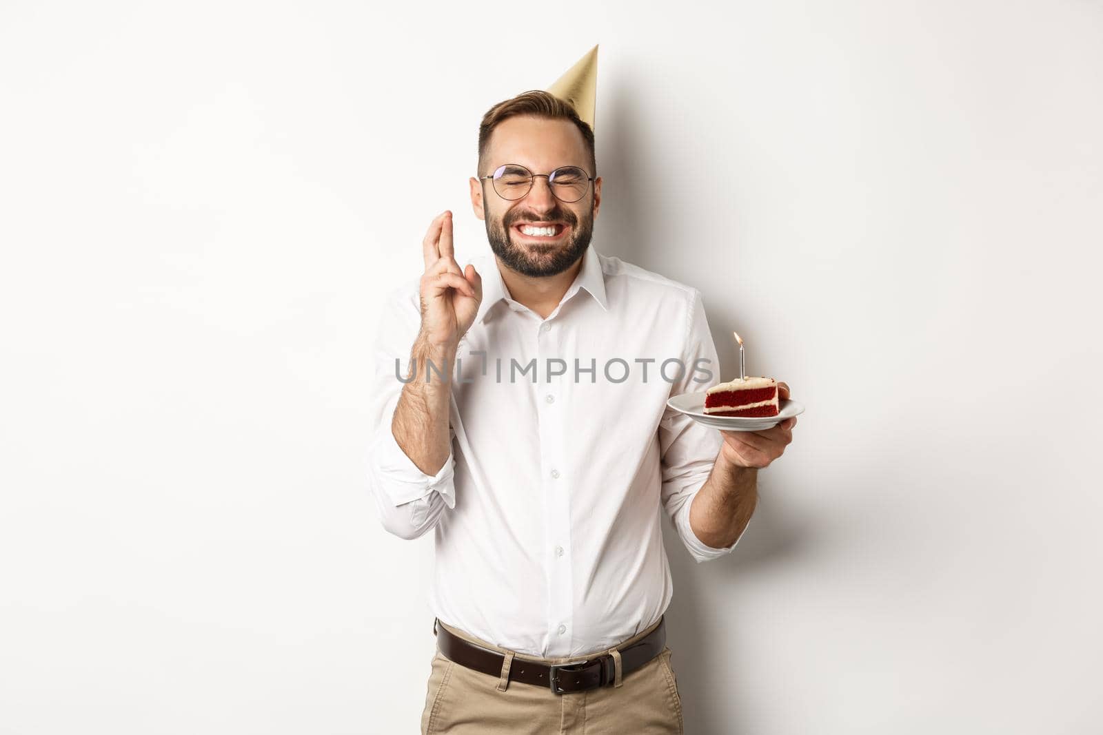 Holidays and celebration. Happy man making wish on birthday cake, cross fingers and smiling excited, having b-day party, white background.