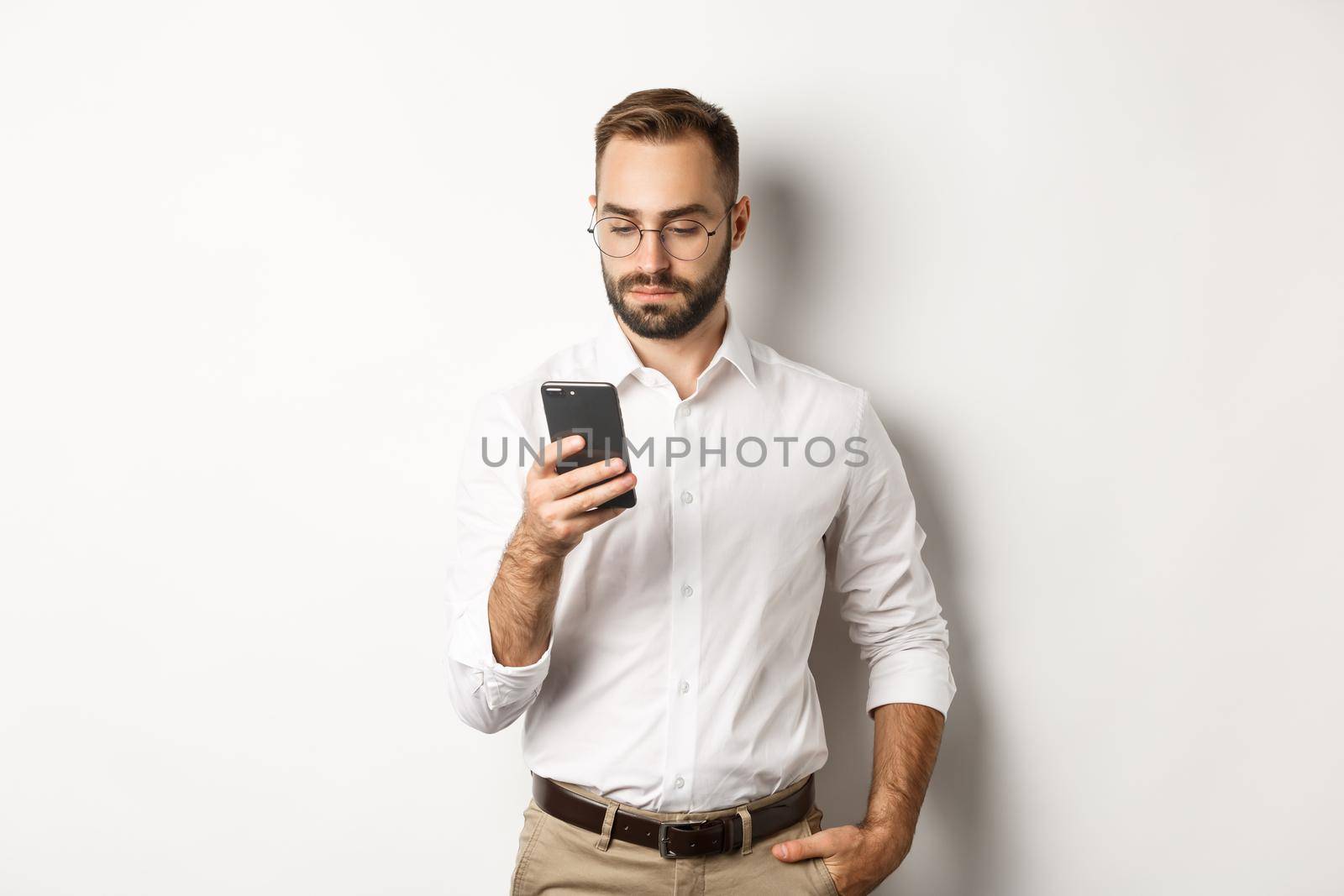 Businessman reading message on phone, standing over white background.