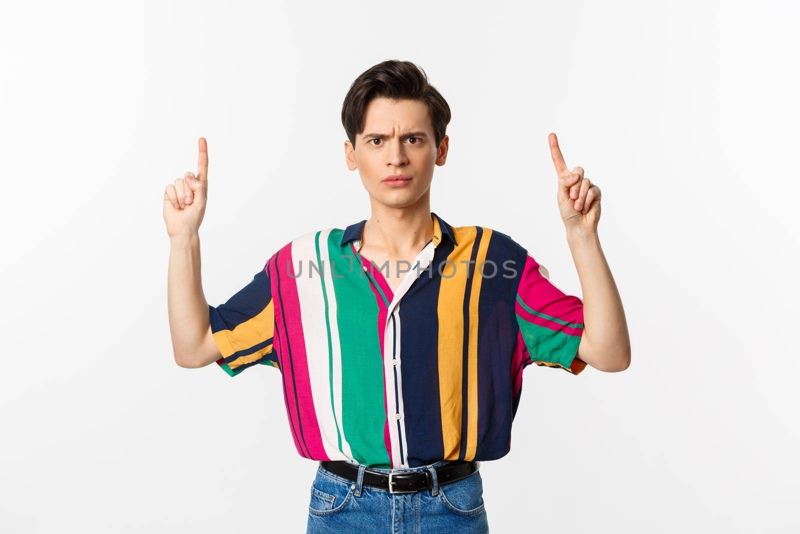 Disappointed and angry man pointing fingers up, showing something bad, standing over white background. Copy space