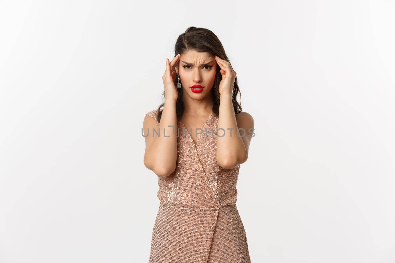 Concept of celebration, holidays and party. Distressed young woman in luxurious dress feeling sick, touching head and grimacing from painful headache, having migraine, white background.