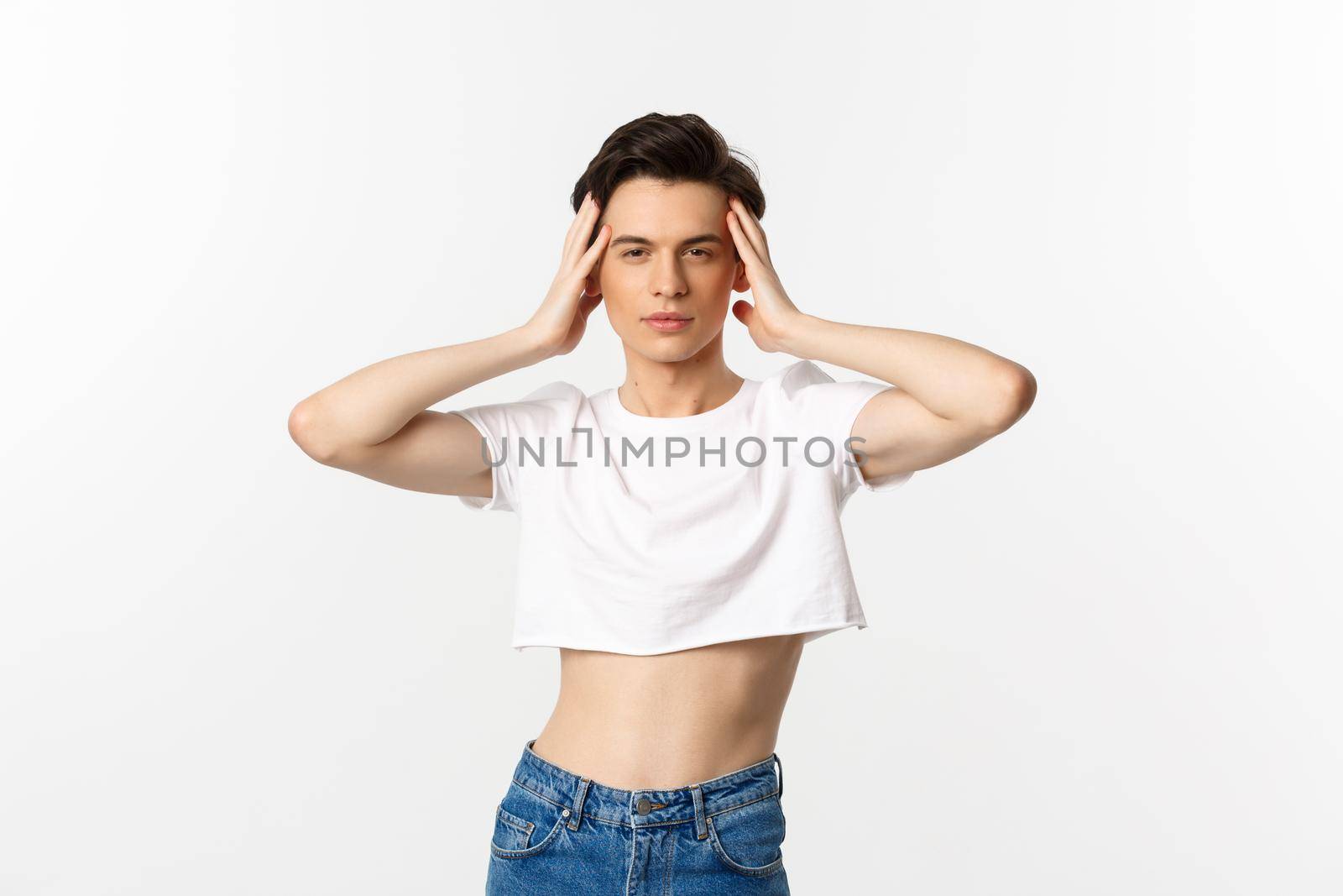 Lgbtq and pride concept. Beautiful and confident gay man wearing crop top, touching face and looking sassy at camera, standing over white background.
